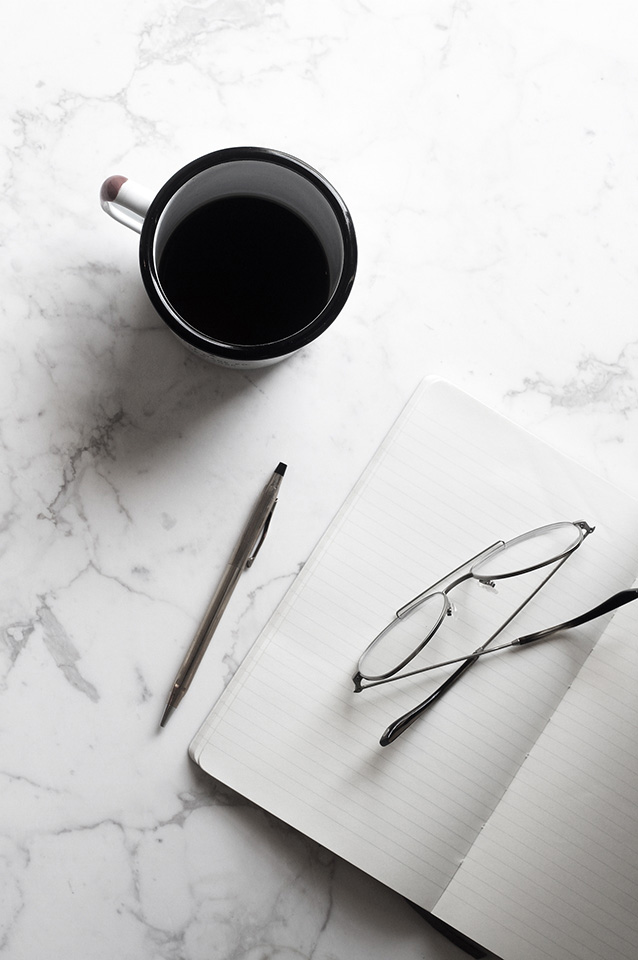 Cup of coffee on a marble background with a notebook and a pen