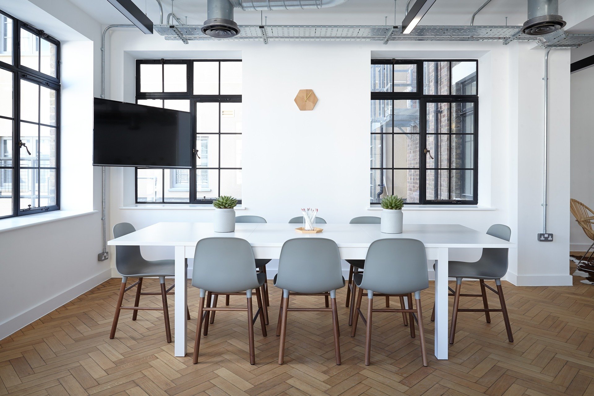 Bright office with a white table in the middle of it and grey chairs around the table